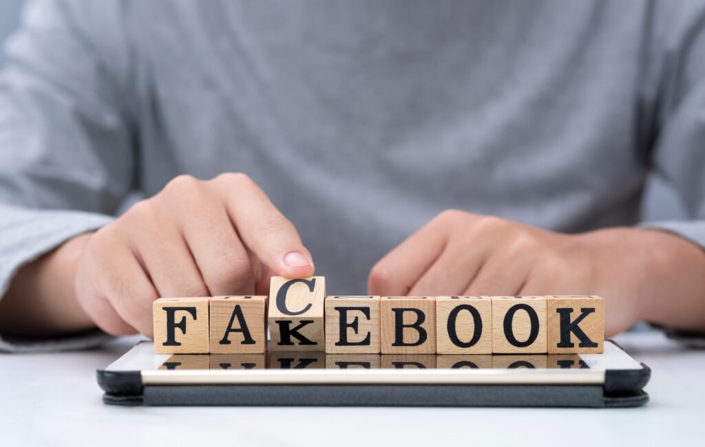 Mão virando texto de madeira para mudar "fakebook" para "facebook" no tablet