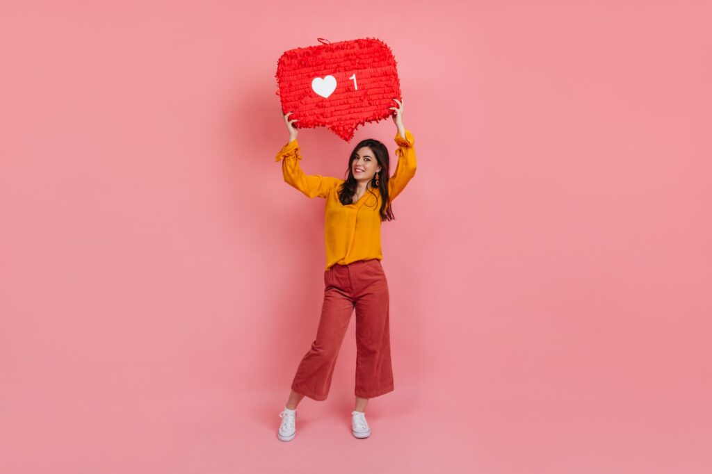 Retrato de corpo inteiro de uma garota alegre em culottes e blusa amarela segurando “curtir” o instagram si
